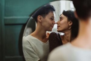 An LGBTQ+ couple looking at each other at a loving manner through a mirror reflection. Trauma counseling in Portland, OR can help individuals heal from PTSD and harmful memories. Get the support you deserve today.