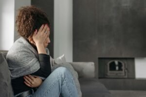 A woman wearing a blanket around her body while sitting on the couch. Representing how PTSD symptoms can interrupt your life. Discover how PTSD counseling in Portland, OR can help you find joy again.
