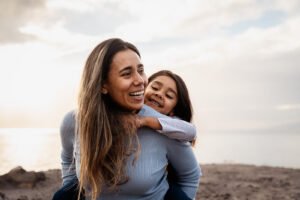 A happy woman carrying her child on her back. Trauma treatment in Portland, OR can help with PTSD & traumatic memories. Healing is possible.
