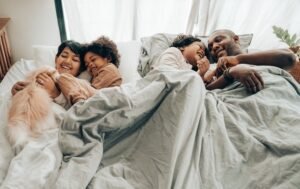 A happy family laying in a large bed together all laughing. Representing how anxiety therapy in Portland, OR can help you get a good nights sleep. Reach out today to start sleeping better. 