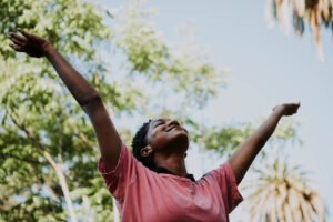 A black woman throwing her hands in the air & smiling outside. Representing how behavioral activation can help you find joy in the little things again. Get started with an anxiety therapist in Portland, OR today!