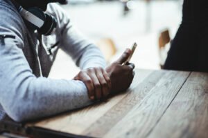 A man looking at his phone while sitting down at a wooden table. Representing how relationship anxiety therapy in Portland, OR can help couples address several challenges. Reach out today to get started.