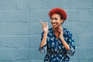 A black woman smiling & pointing to the air while standing in front of a blue brick wall. Struggle with procrastination & time management? Learn tips in our anxiety treatment in Portland, OR. 