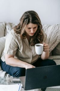 A woman holding a coffee mug while typing away on her computer. If you struggle with procrastination, reach out to us today to begin therapy for anxiety in Portland, OR. Get in touch now!