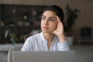 A woman holding her head in one arm while looking away from her computer. Representing how perfectionism can cause stress & anxiety. Get started with our anxiety therapy in Portland, OR to find delegation strategies!