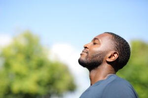 A man standing outdoors with his eyes closed, appearing calm and reflective, representing mindful connection to emotions and body awareness.
