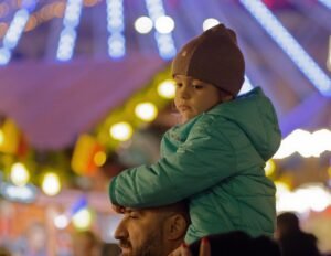 Child sitting on adult’s shoulders at a brightly lit event, appearing anxious—highlighting how anxiety in children may be mistaken for moodiness or defiance.