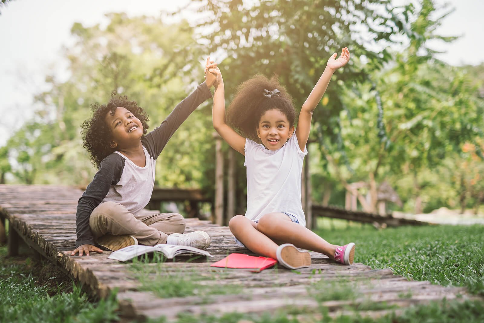 Two kids holding hands in victory outside on a wooden path. If your child struggles with anxiety, reach out today for anxiety therapy in Portland, OR. Get paired with a therapist today.