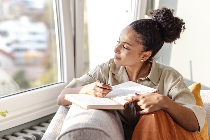A person writing in a journal while seated in a calm space, reflecting on emotions and personal experiences.
