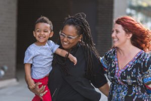 Two parents smiling and holding their young child outdoors, capturing a joyful and present parenting moment