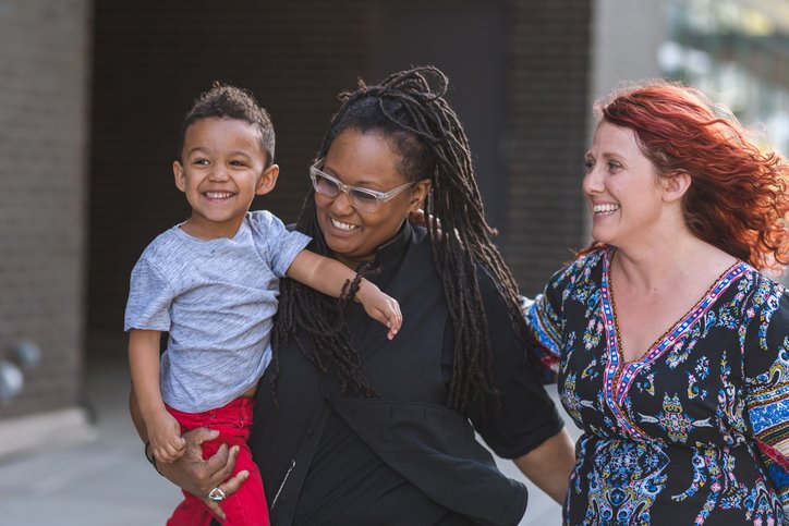 Two parents smiling and holding their young child outdoors, capturing a joyful and present parenting moment