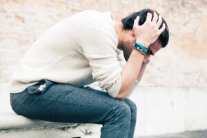 A man wearing colorful bracelets sitting holding his head. Did you know unprocessed trauma can affect your mind & body? Discover how trauma treatment in Portland, OR can help you find relief. Call today!