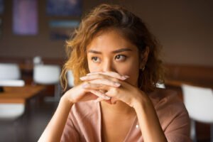An Asian woman holding her hands to her mouth covering half of her face. Representing how trauma counseling in Portland, OR can help with trauma bonds. Learn more by reading our blog.