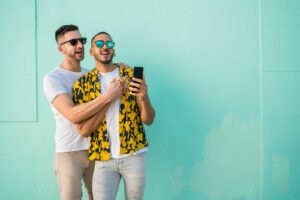 A happy biracial gay couple smiling in front of a mint green wall. Trauma treatment in Portland, OR can help you build healthy relationships. Let go of a trauma bond today.