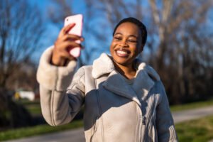 A happy Black woman smiling at her phone while walking outside. If unprocessed trauma is affecting your life, our trauma therapists in Portland, OR can help. Find relief today with compassionate support. 