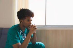 A young Black male nurse sitting alone in a room, thinking. If trauma is affecting your everyday life, reach out to us today. We offer compassionate trauma therapy in Portland, OR.