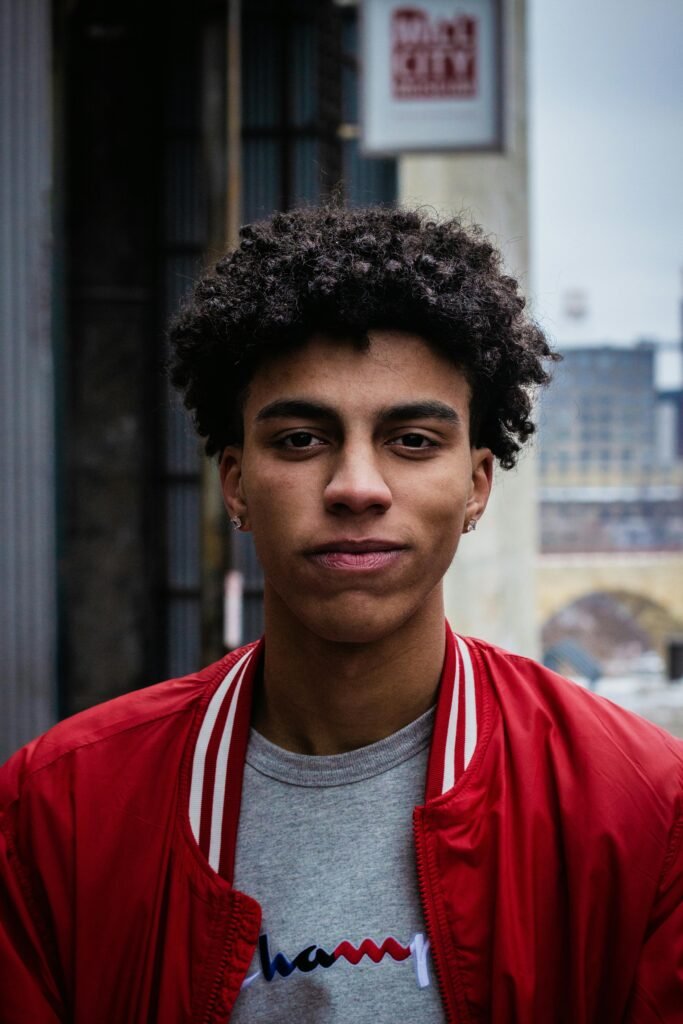 Confident young adult standing in an urban setting wearing a red jacket and gray t-shirt, symbolizing self-assurance and representation in LGBTQIA+ affirming therapy in Portland, Oregon.