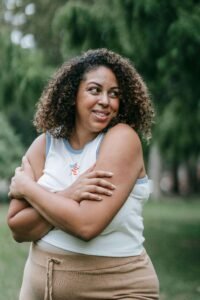A Black woman smiling and hugging herself with compassion. Representing how our trauma-informed care can help you heal. Contact us today to get started with a trauma therapist in Portland, OR. 