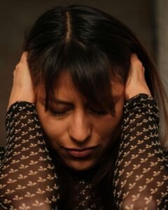 A woman wearing a black & white long sleeve is covering her ears in fear. Representing how trauma can affect you mentally, physically & emotionally. Reach out today to start healing with trauma counseling in Portland, OR. 
